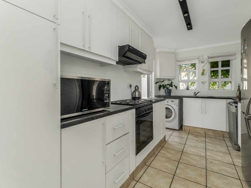 A functional kitchen featuring white cabinetry, granite countertops, integrated appliances, and tiled flooring with a dedicated laundry area.