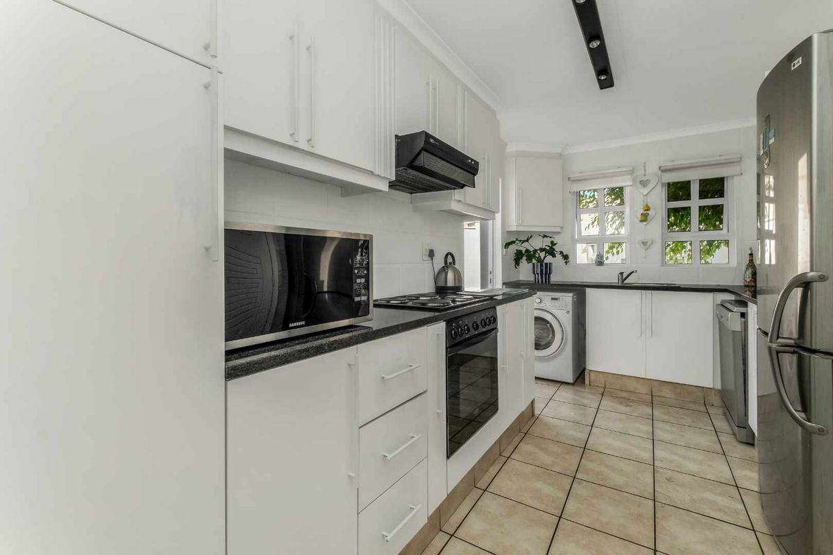 A functional kitchen featuring white cabinetry, granite countertops, integrated appliances, and tiled flooring with a dedicated laundry area.