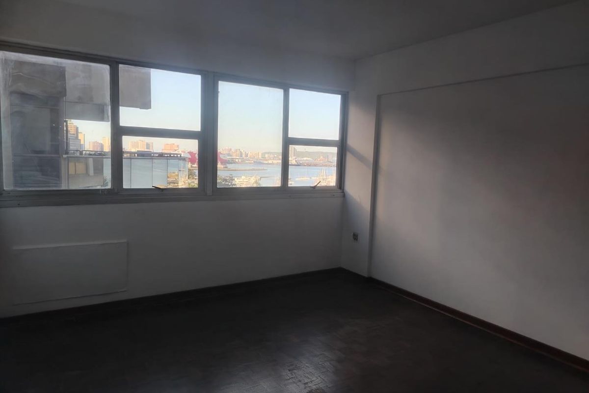 An empty bedroom featuring parquet flooring and large windows that offer a scenic harbor and city view.