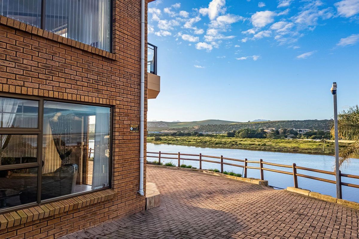 Exterior view of the apartment building featuring brick facade, paved patio area, and scenic riverfront outlook.