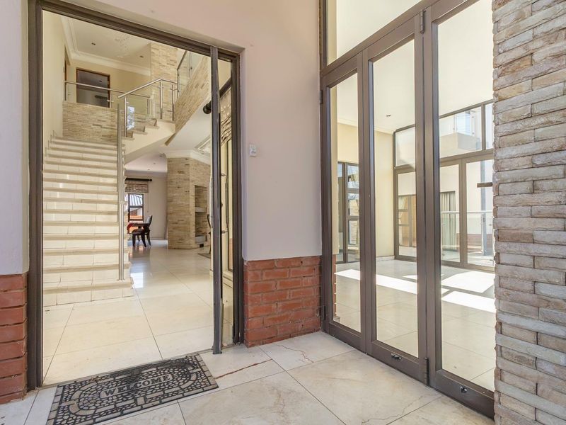 Spacious entrance hall featuring modern tiled flooring, stone-clad accents, and a striking staircase with a glass balustrade leading to the upper level.