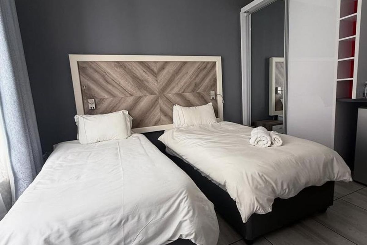 A modern hotel bedroom featuring twin beds, a decorative wood-panel headboard, and a built-in sliding door wardrobe with integrated shelving.