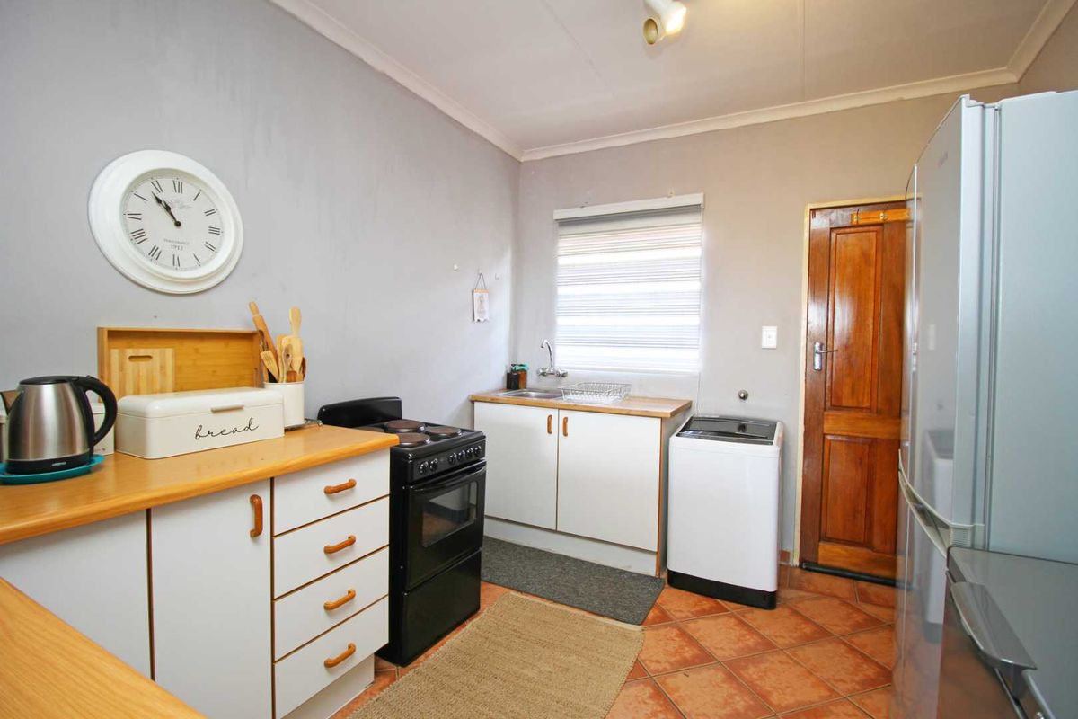 A functional kitchen featuring white cabinetry, a freestanding stove, a single basin sink, and tiled flooring with direct access to an exterior door.
