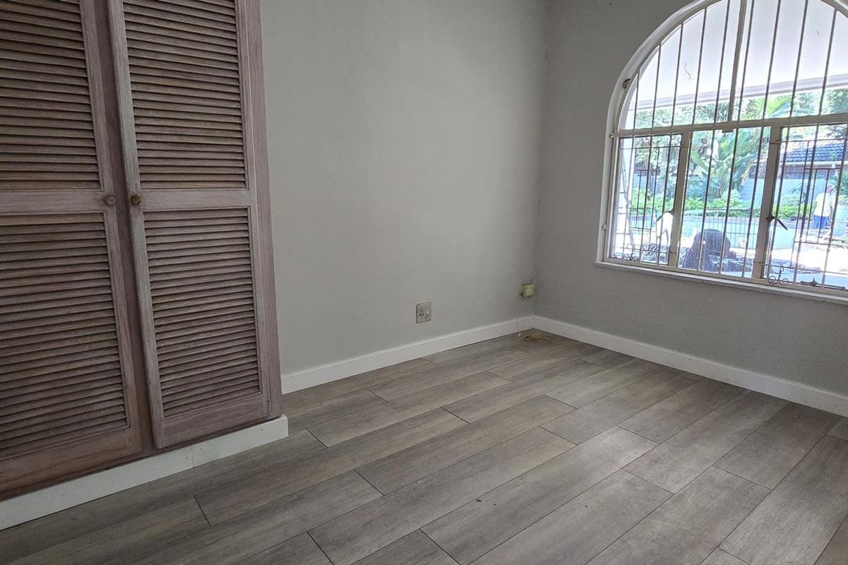 A bedroom featuring light wood-look flooring, built-in louvered-door cupboards, and an arched window with security bars.