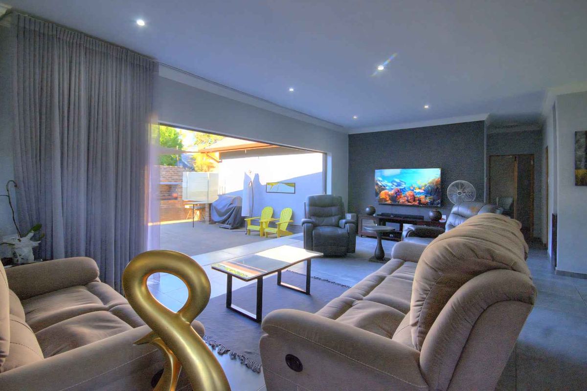 Spacious living room featuring large sliding glass doors that open to an outdoor patio, tiled floors, and a modern feature wall.