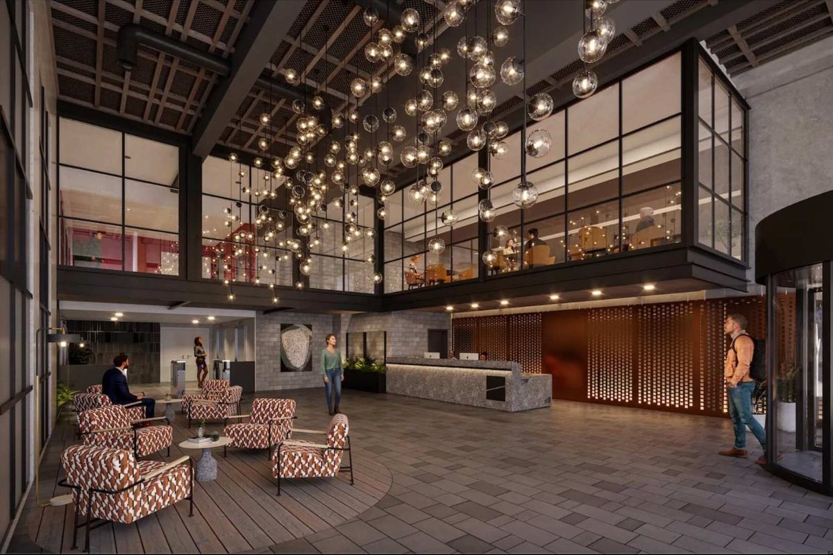 Modern industrial-style lobby featuring a stone reception desk, mezzanine level with glass partitioning, and dramatic decorative pendant lighting.