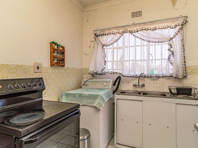 A dated kitchen featuring a built-in stove, double sink, and tiled splashback, currently showing significant signs of wear and wall damage.