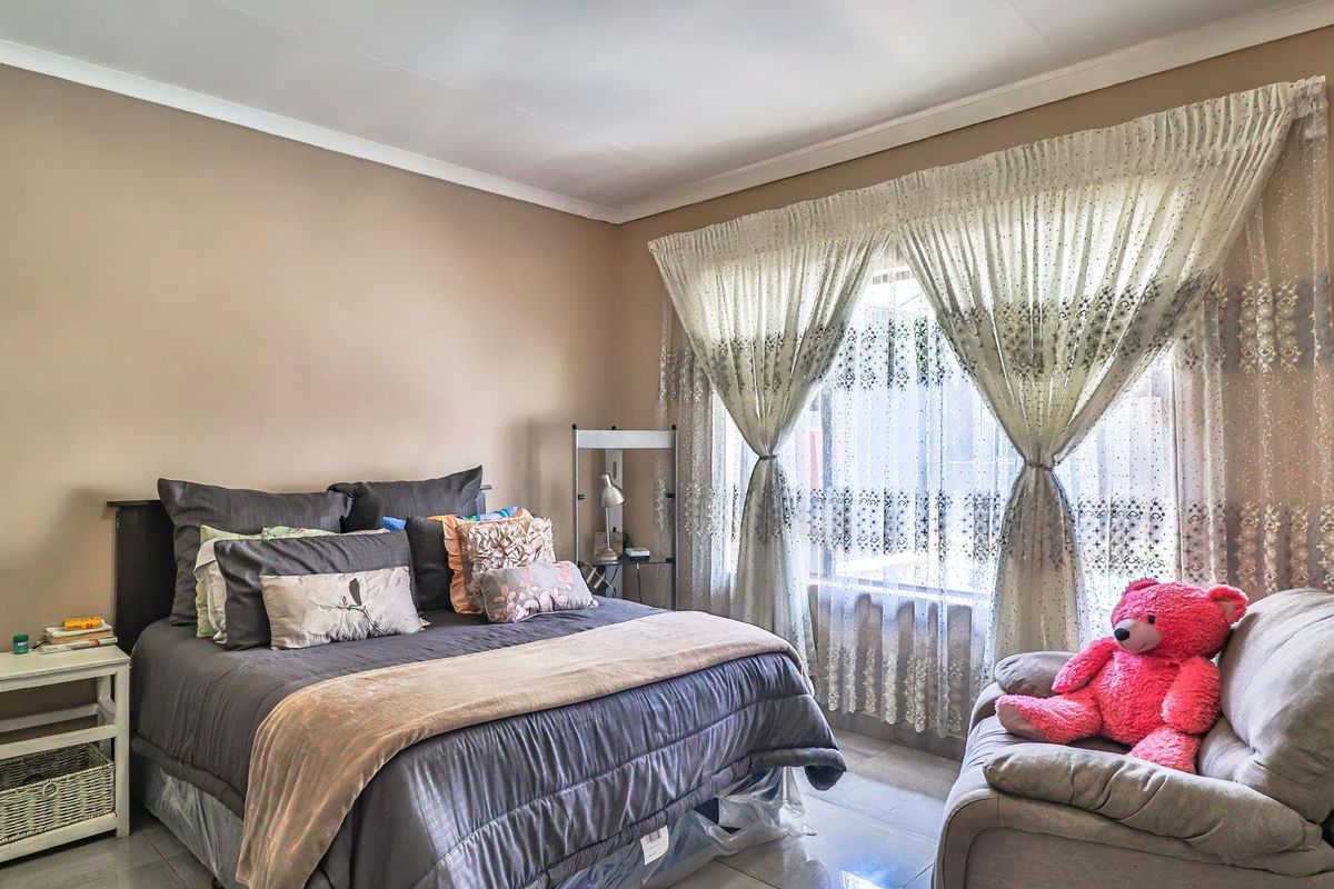A well-lit bedroom featuring tiled flooring, neutral wall tones, and large windows dressed with classic curtains, providing a comfortable and functional living space.