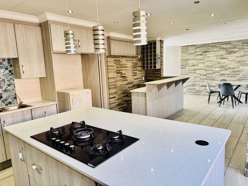 Modern open-plan kitchen featuring a central island with gas hob, stone countertops, breakfast bar, and stylish stone cladding feature walls.