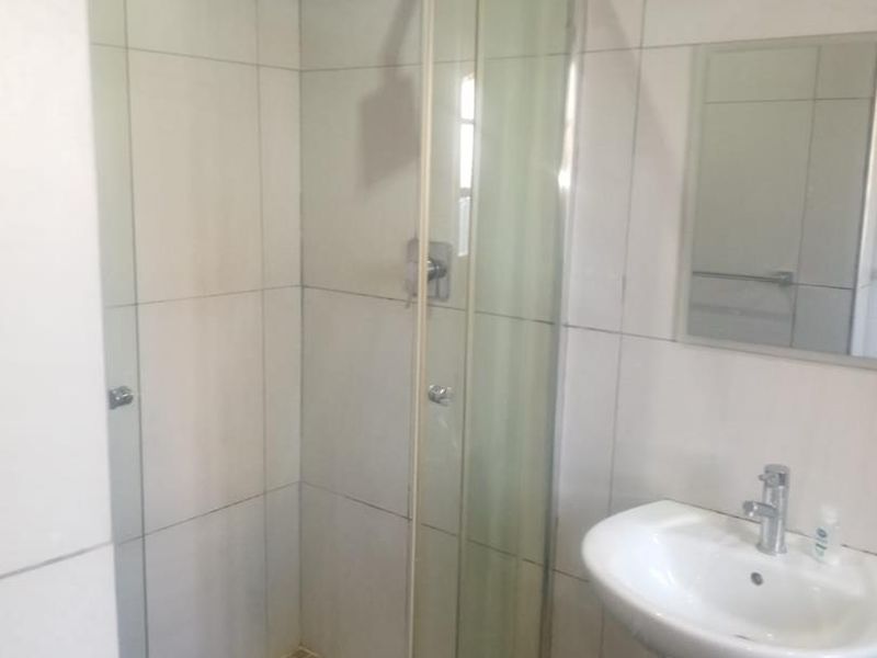 A functional bathroom featuring a curved glass shower enclosure, pedestal basin, and neutral wall tiling, offering a clean and practical layout.