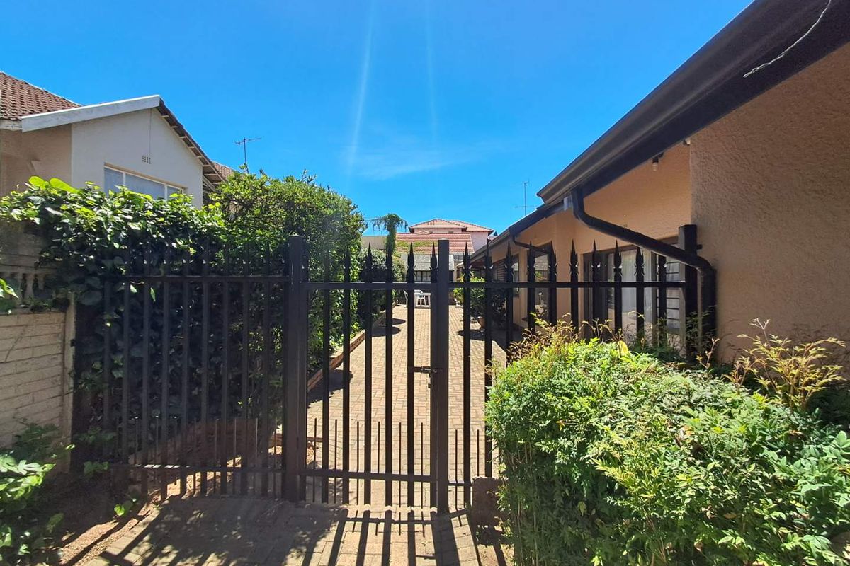 A secure side access path featuring a metal gate, paved driveway, and established garden borders between two residential structures.