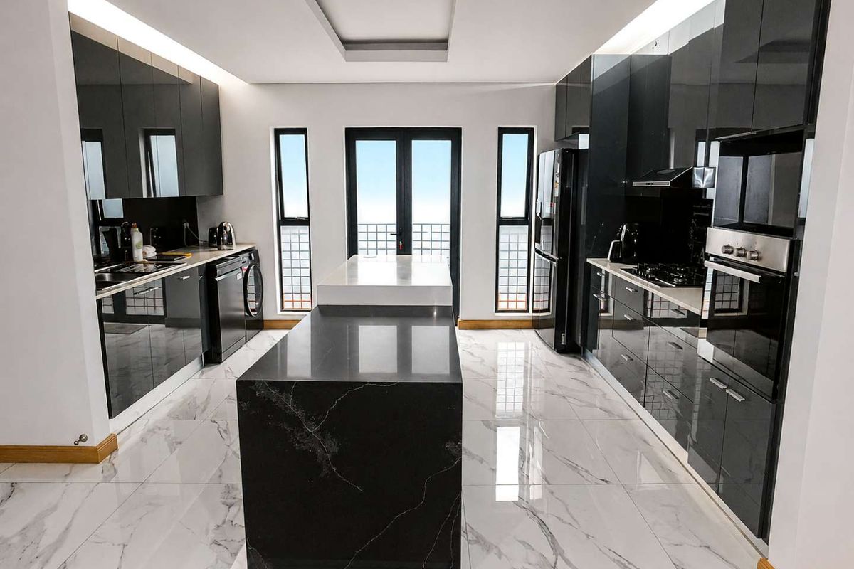 Modern kitchen featuring high-gloss black cabinetry, a central island with stone countertop, marble-look floor tiles, and integrated appliances.