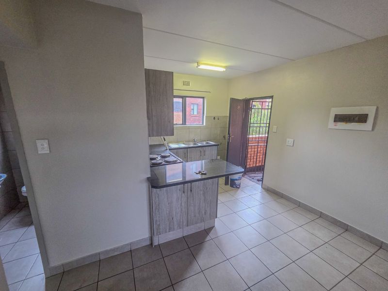 A functional kitchen featuring built-in cabinetry, a breakfast counter, electric hob, and tiled flooring, with direct access to an exterior security gate.