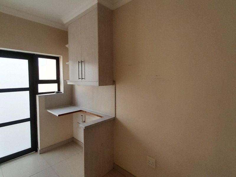 A functional laundry area featuring built-in cabinetry, a countertop with plumbing connections, and direct access to the exterior via an aluminium framed door.