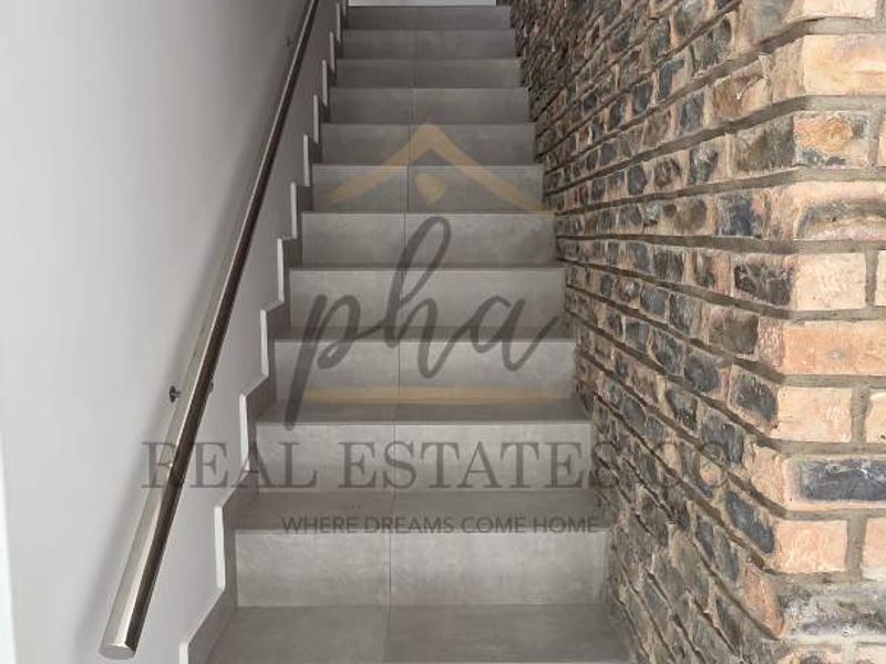 A modern staircase featuring large format grey floor tiles, a sleek stainless steel handrail, and a striking exposed brick feature wall.
