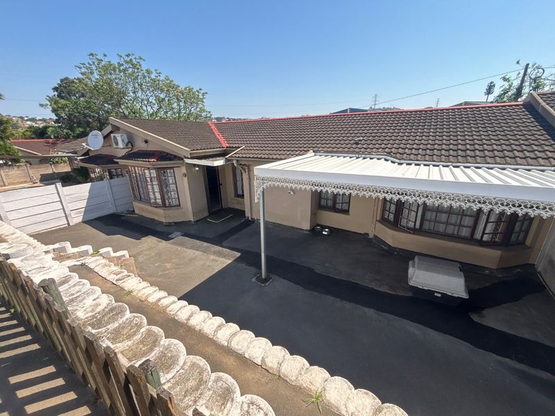 Rear exterior view of the townhouse featuring a tiled roof, covered patio area with decorative trim, bay windows, and a paved driveway.