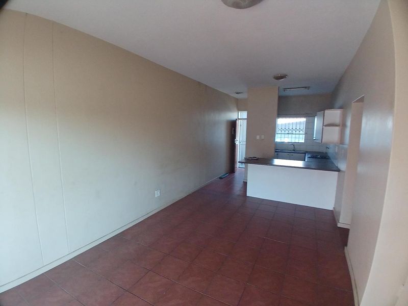 An open-plan living and kitchen area featuring tiled flooring, a breakfast bar, and basic kitchen cabinetry in a vacant apartment setting.