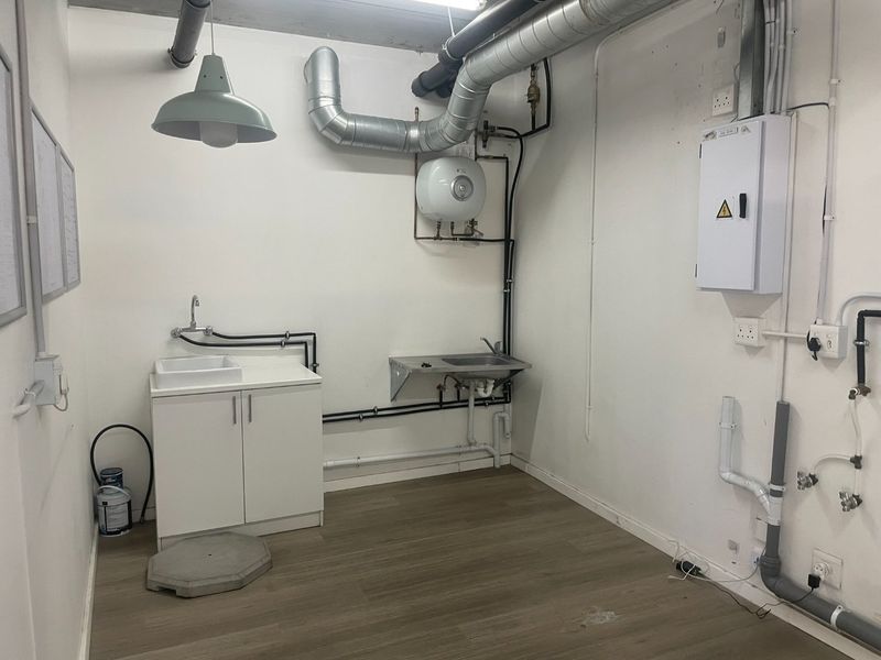 A functional utility space featuring a sink, cabinetry, water heater, and exposed industrial-style ducting and piping, suitable for storage or service requirements.