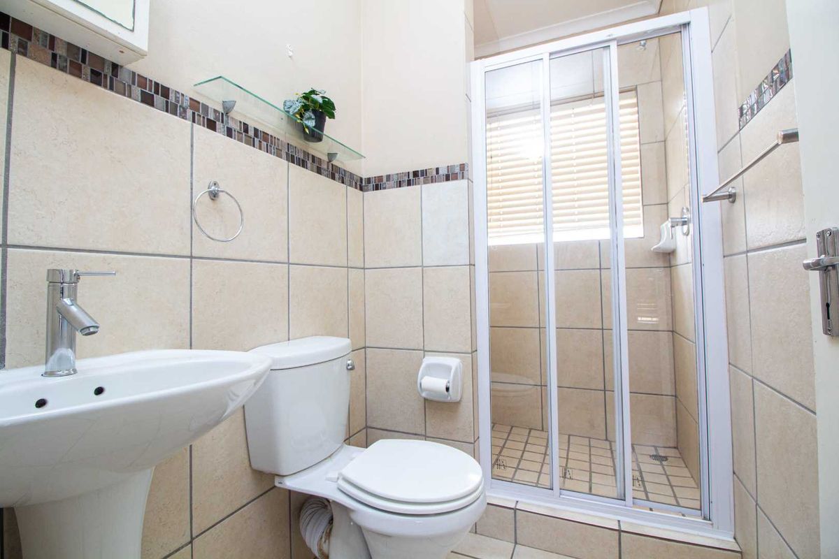 A functional bathroom featuring a pedestal basin, a standard toilet, and a tiled shower enclosure with sliding glass doors.