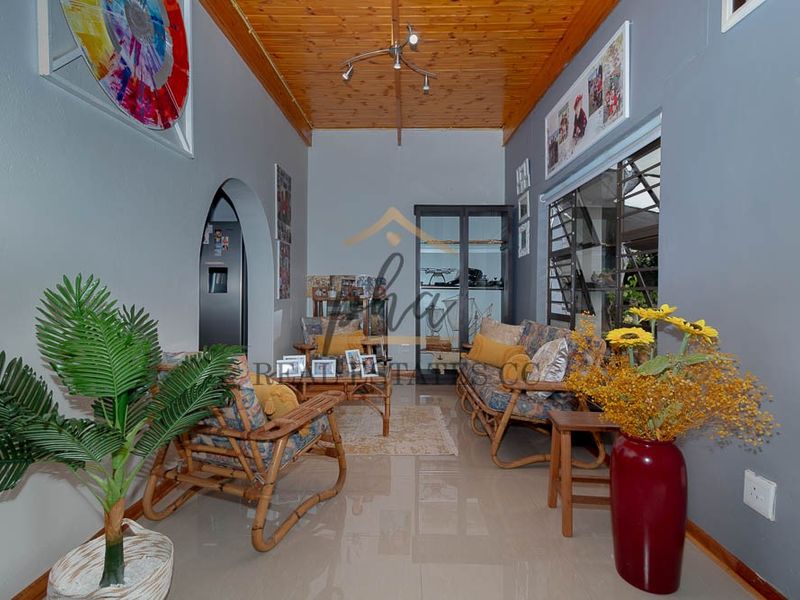 A living room featuring a timber-paneled ceiling, tiled flooring, and an arched doorway leading to adjacent spaces.