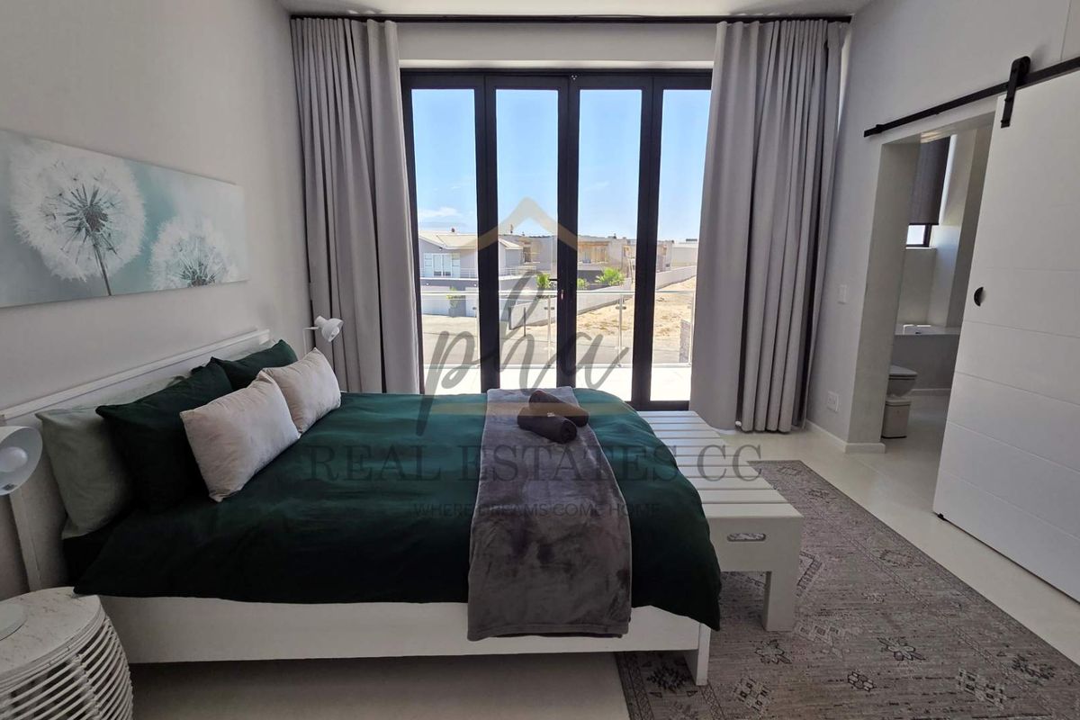 Modern bedroom featuring large glass sliding doors leading to a balcony, neutral finishes, and an en-suite bathroom accessed via a sliding barn door.