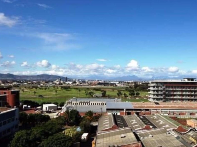 An elevated panoramic view overlooking the surrounding urban landscape, industrial buildings, and distant mountain ranges under a clear blue sky.