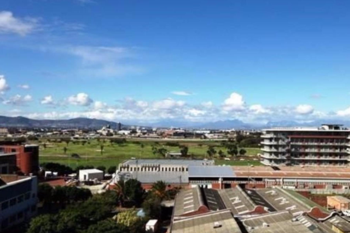 An elevated panoramic view overlooking the surrounding urban landscape, industrial buildings, and distant mountain ranges under a clear blue sky.