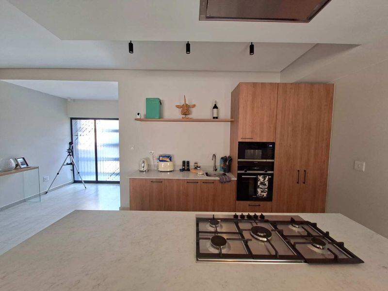 Modern kitchen featuring a central island with a gas hob, built-in oven and microwave, stone countertops, and sleek wooden cabinetry.
