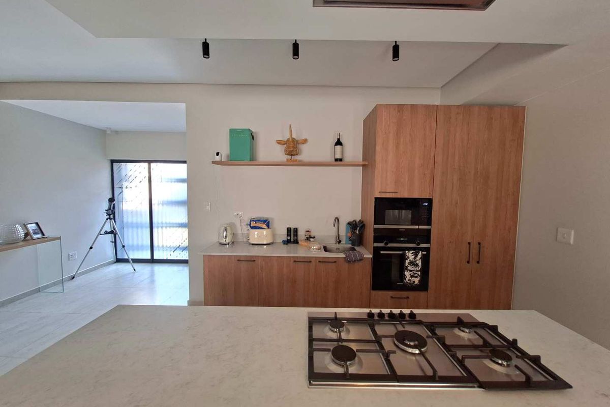 Modern kitchen featuring a central island with a gas hob, built-in oven and microwave, stone countertops, and sleek wooden cabinetry.