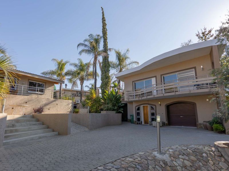 Front exterior view of a multi-level house featuring a paved driveway, concrete staircase, retaining walls, and a balcony above the garage.