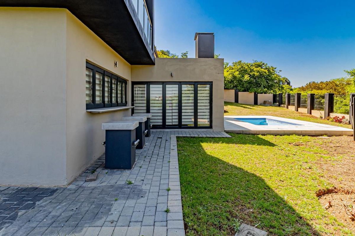 Rear exterior view featuring a paved patio area, built-in outdoor counter, swimming pool, and landscaped garden with perimeter walling.