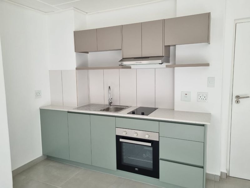 A modern, clean kitchen featuring sage green lower cabinets, neutral upper cabinetry, stone countertops, and integrated stainless steel appliances.