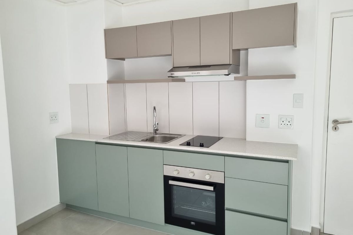 A modern, clean kitchen featuring sage green lower cabinets, neutral upper cabinetry, stone countertops, and integrated stainless steel appliances.