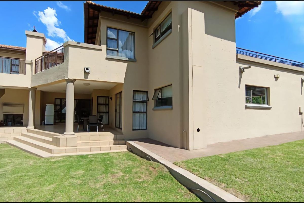 Rear view of the house featuring a covered patio, tiled steps, upper balcony with metal railings, and a well-maintained lawn.