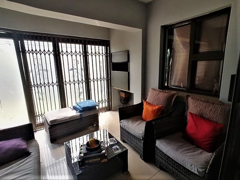 A bright living area featuring tiled flooring, large sliding doors with security gates, and a recessed wall niche for storage or display.