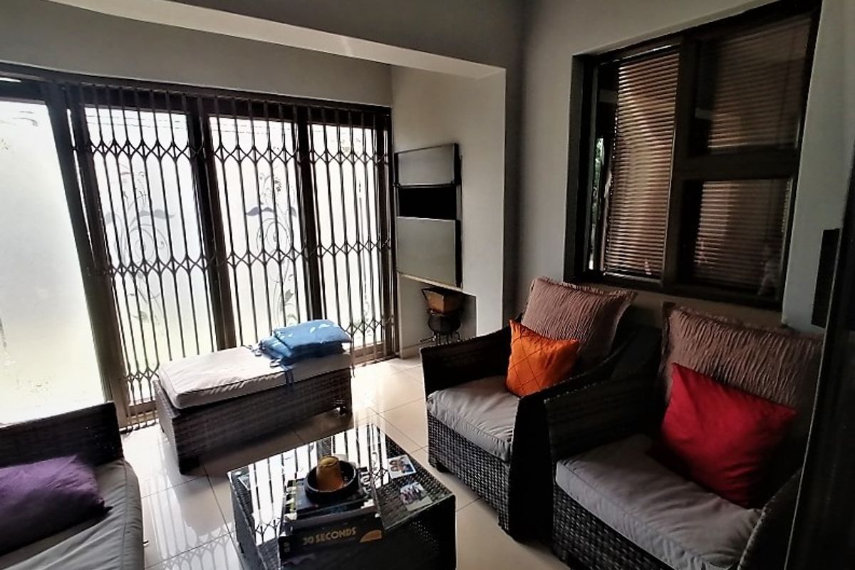 A bright living area featuring tiled flooring, large sliding doors with security gates, and a recessed wall niche for storage or display.