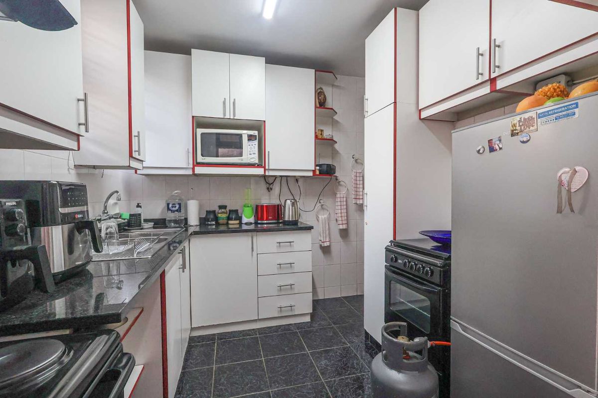 A compact kitchen featuring white cabinetry with red trim, dark granite countertops, tiled flooring, and a built-in microwave space.