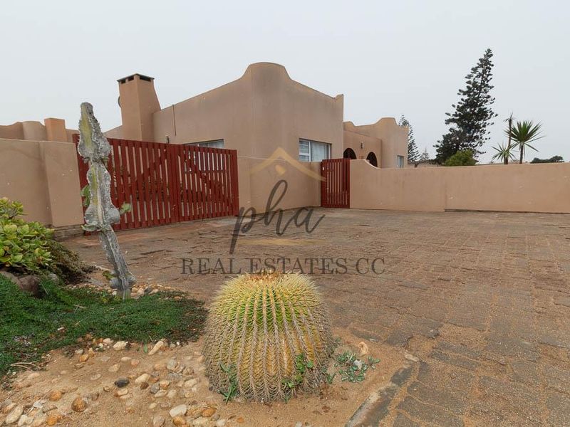 Front exterior view of the property featuring a paved driveway, boundary wall, and timber gate access.
