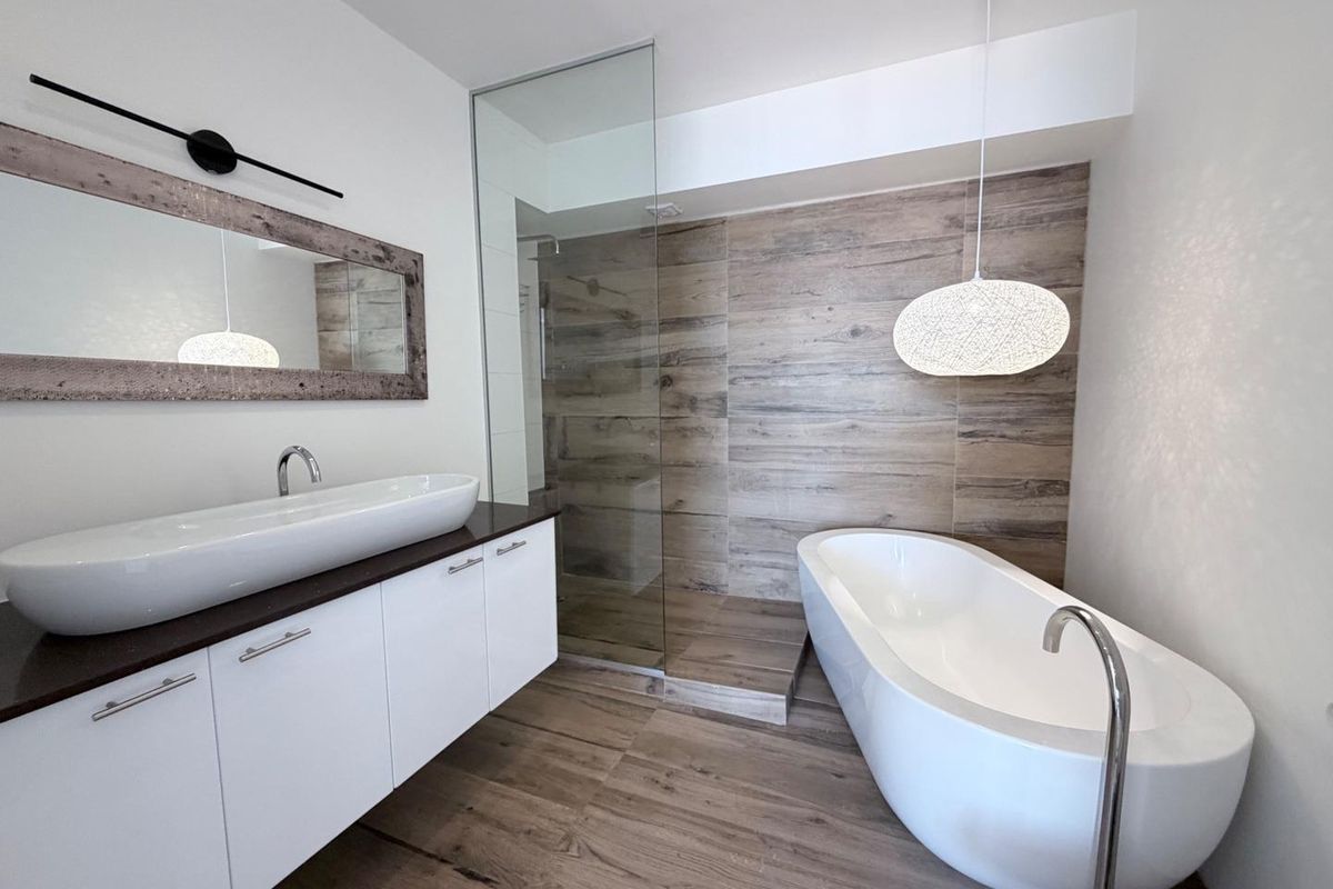Modern bathroom featuring a freestanding bathtub, walk-in glass shower, wall-mounted vanity with vessel sink, and wood-look tile flooring.
