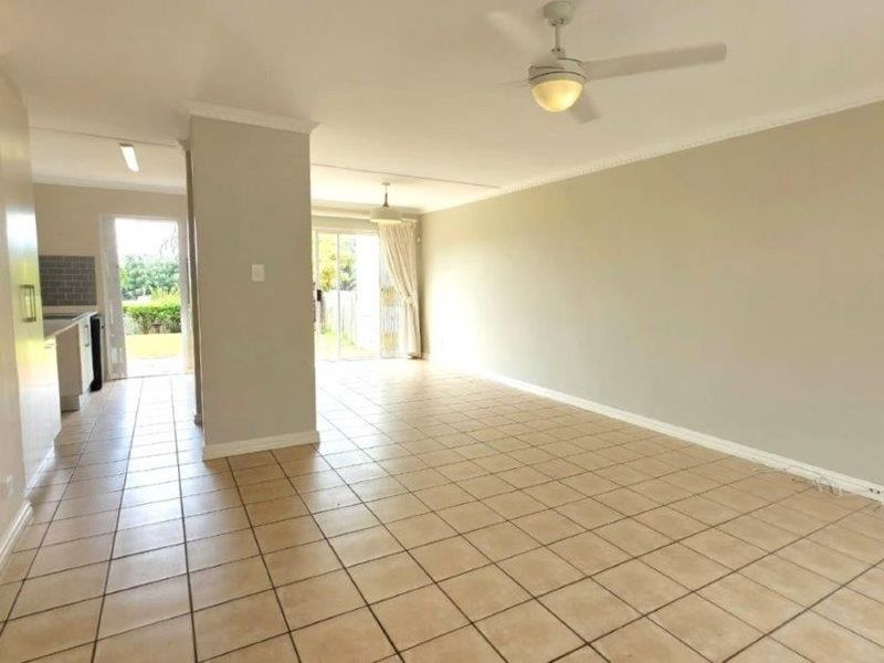 Spacious open-plan living and kitchen area featuring neutral tiled flooring, ceiling fans, and direct access to the outdoor space through sliding glass doors.