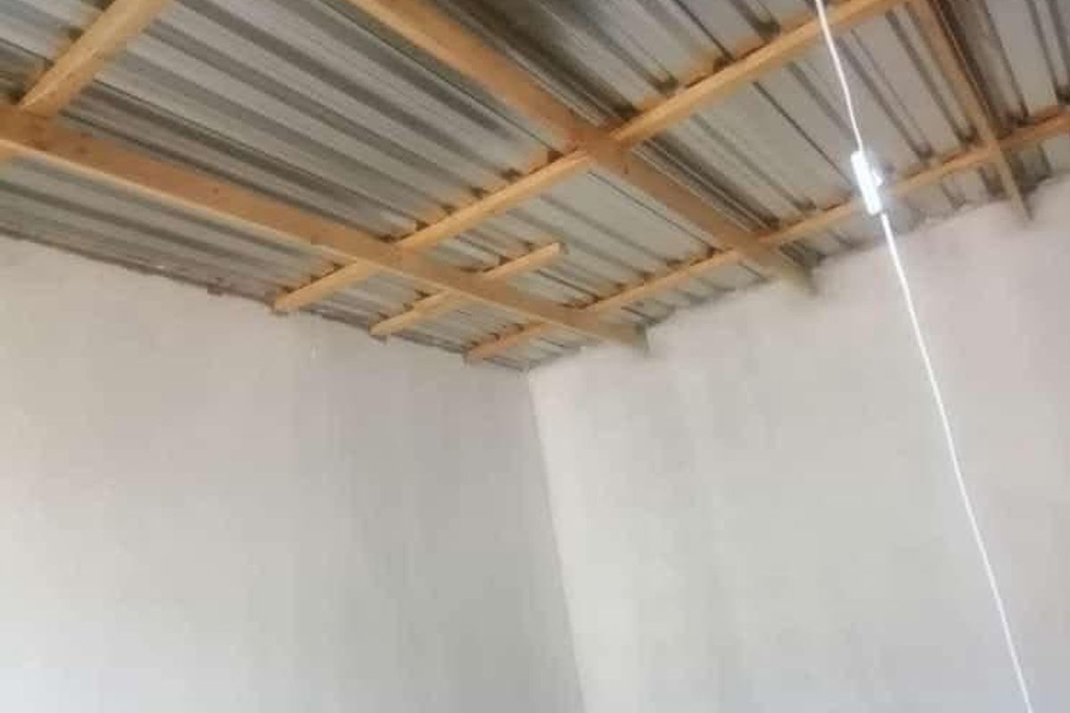An unfinished interior space featuring exposed timber roof trusses and corrugated metal roofing, suitable for renovation or completion.