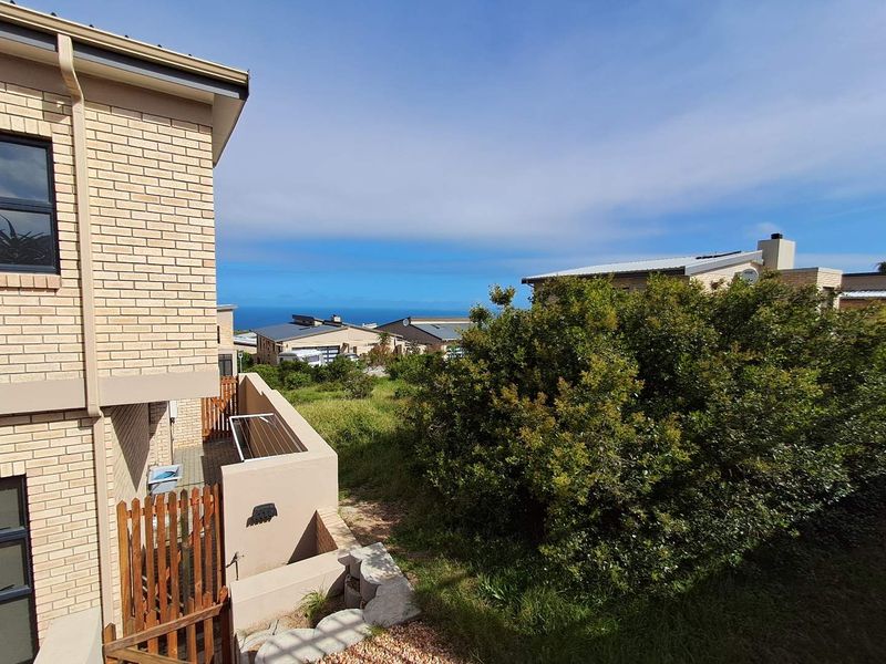 Rear view of the property showing a brick facade, timber gate, and retaining wall with a view towards the ocean.