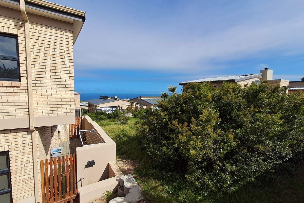 Rear view of the property showing a brick facade, timber gate, and retaining wall with a view towards the ocean.