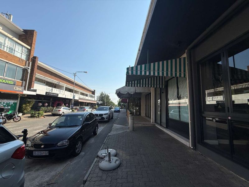Street-level view of a retail storefront featuring paved sidewalk access, large glass display windows, and striped fabric awnings.