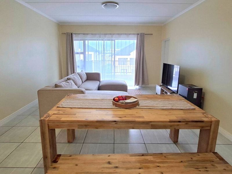 Open-plan living and dining area featuring neutral wall tones, tiled flooring, and a large sliding glass door providing access to the balcony.