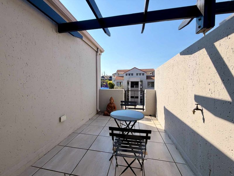 A private balcony featuring tiled flooring, a timber pergola structure, and an exterior water tap, offering an open outdoor space.