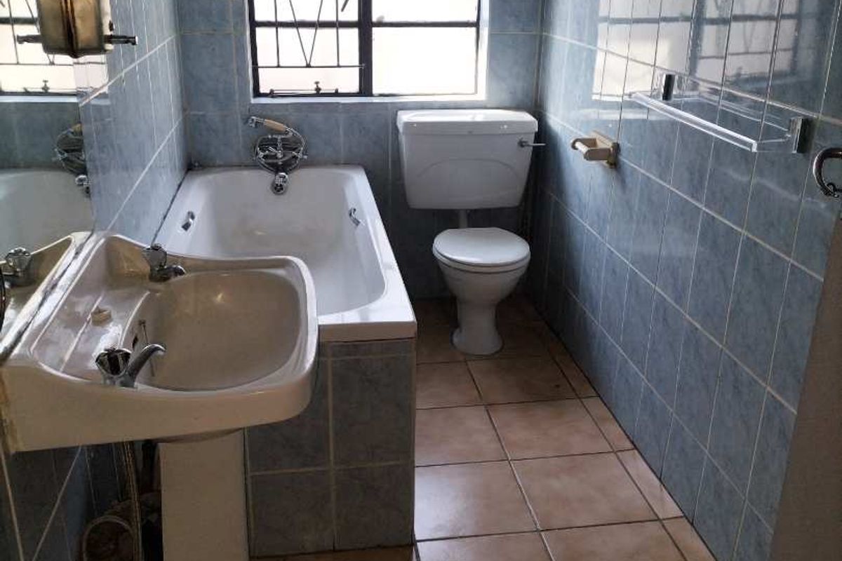 A dated bathroom featuring a pedestal basin, bathtub, and toilet with blue wall tiling and ceramic floor tiles.