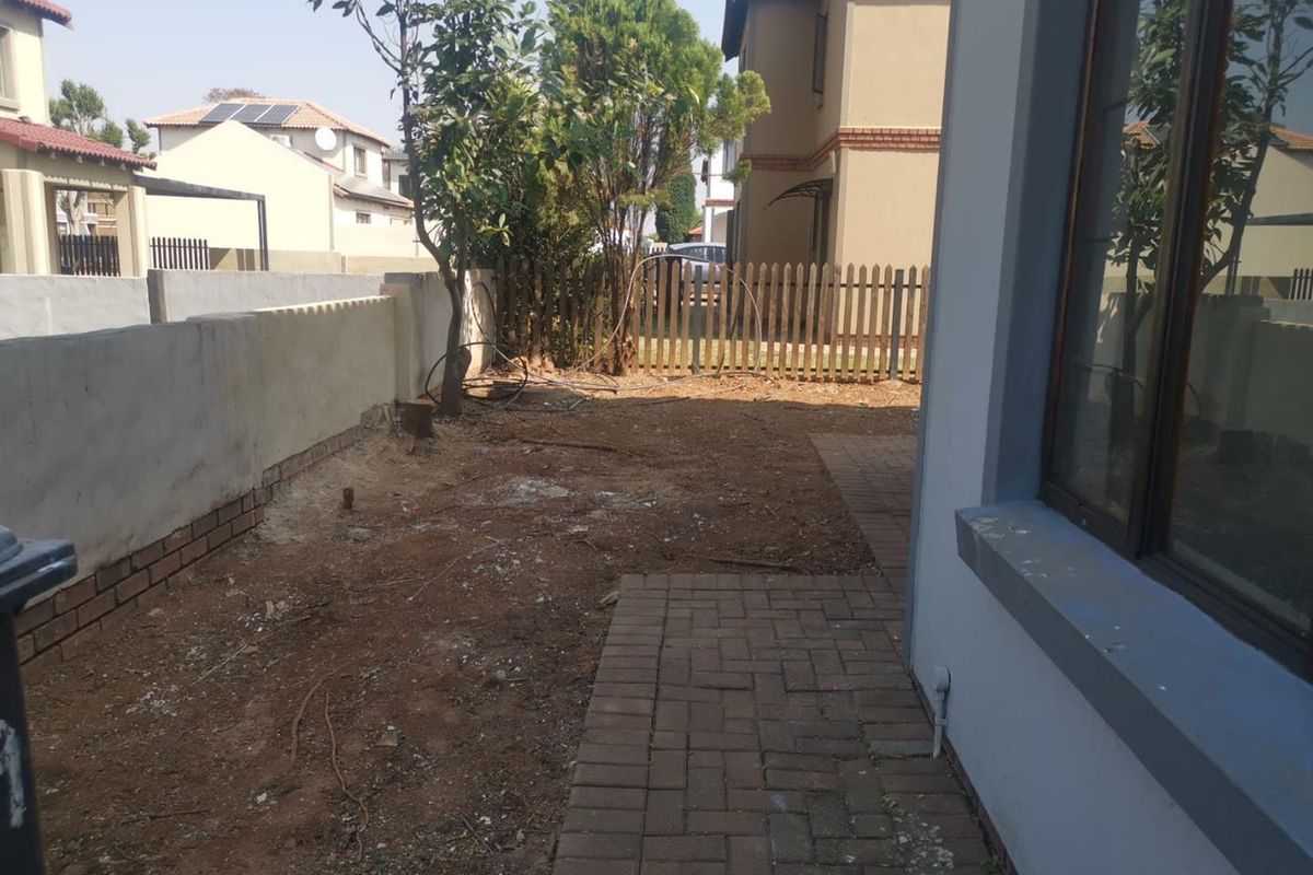 A rear garden area featuring a paved walkway, boundary wall, and wooden fencing, currently requiring landscaping and maintenance to improve the outdoor space.