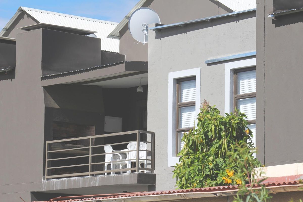 Exterior view of a townhouse featuring a covered balcony with a built-in braai area and modern grey facade finishes.