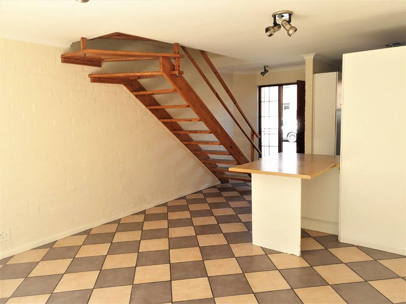 Open-plan living area featuring a wooden staircase, tiled flooring, and a breakfast bar, offering a functional layout ready for personalization.